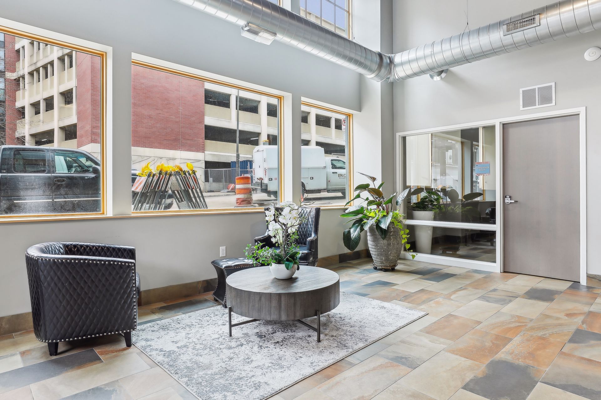 Lobby with seating area, large windows overlooking street, neutral color scheme, stone floor, potted plants.