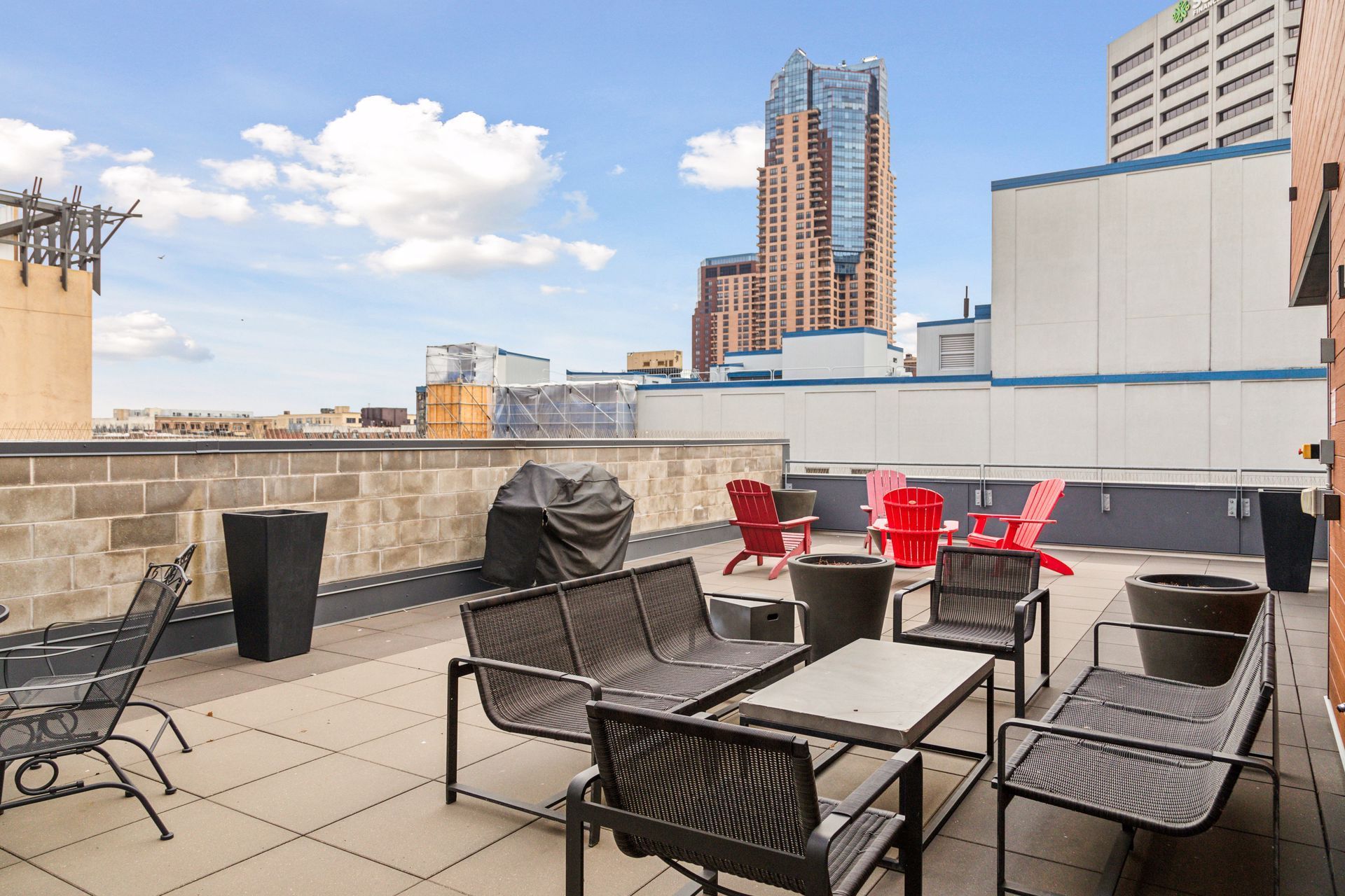 Rooftop patio with seating, grilling area, and city skyline view on a sunny day.