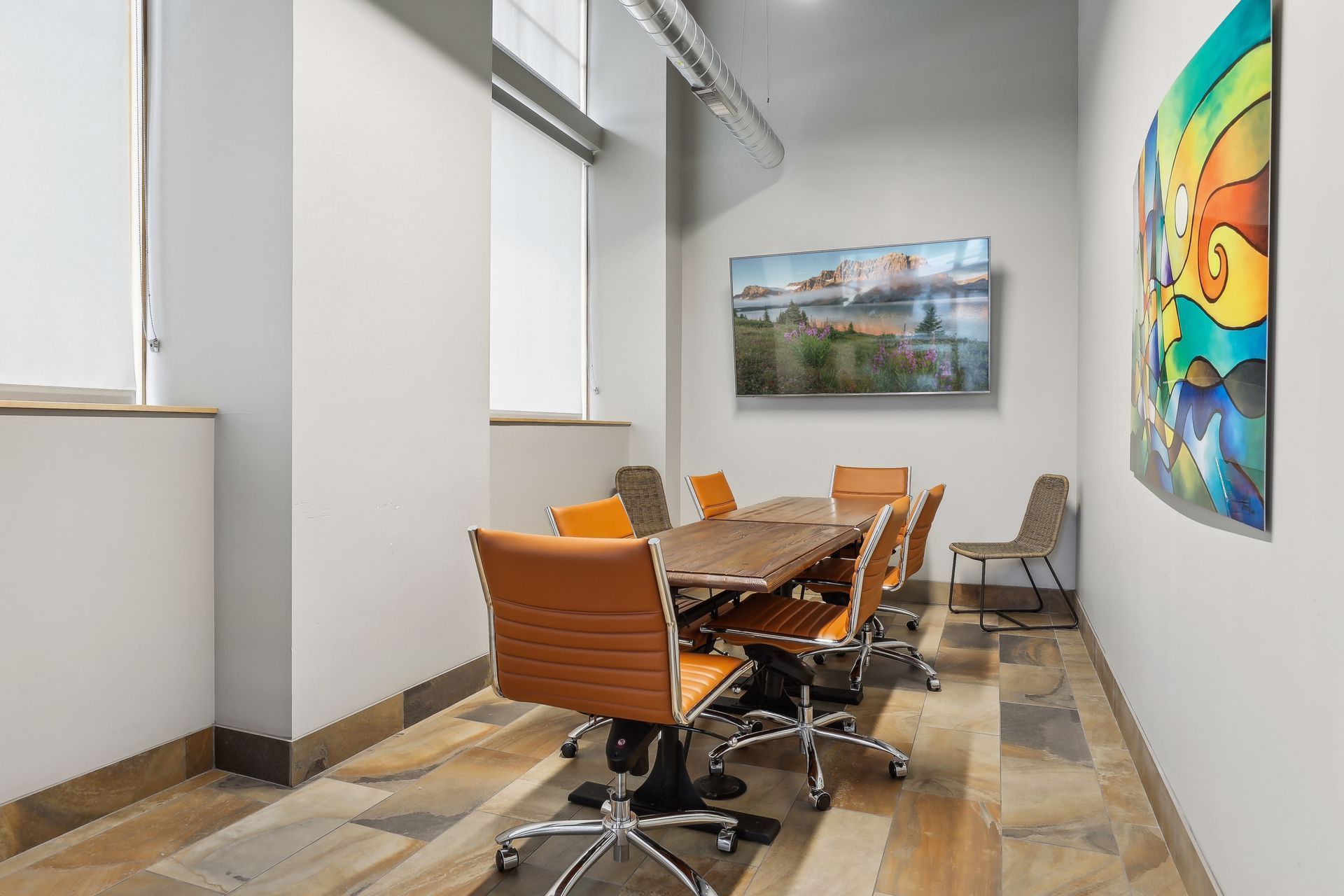 Conference room with table, chairs, TV screen, and colorful abstract art on the wall.