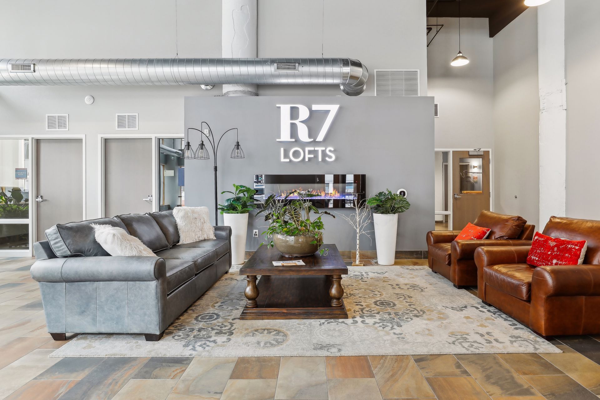 Lobby with seating, fireplace, and R7 Lofts logo. Gray, wood, and leather furnishings.