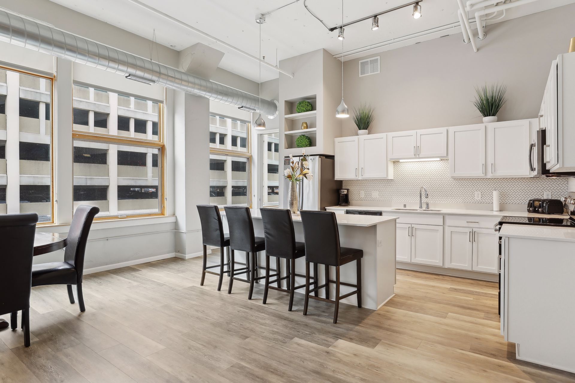 Bright, modern kitchen with white cabinets, island with stools, and large windows.