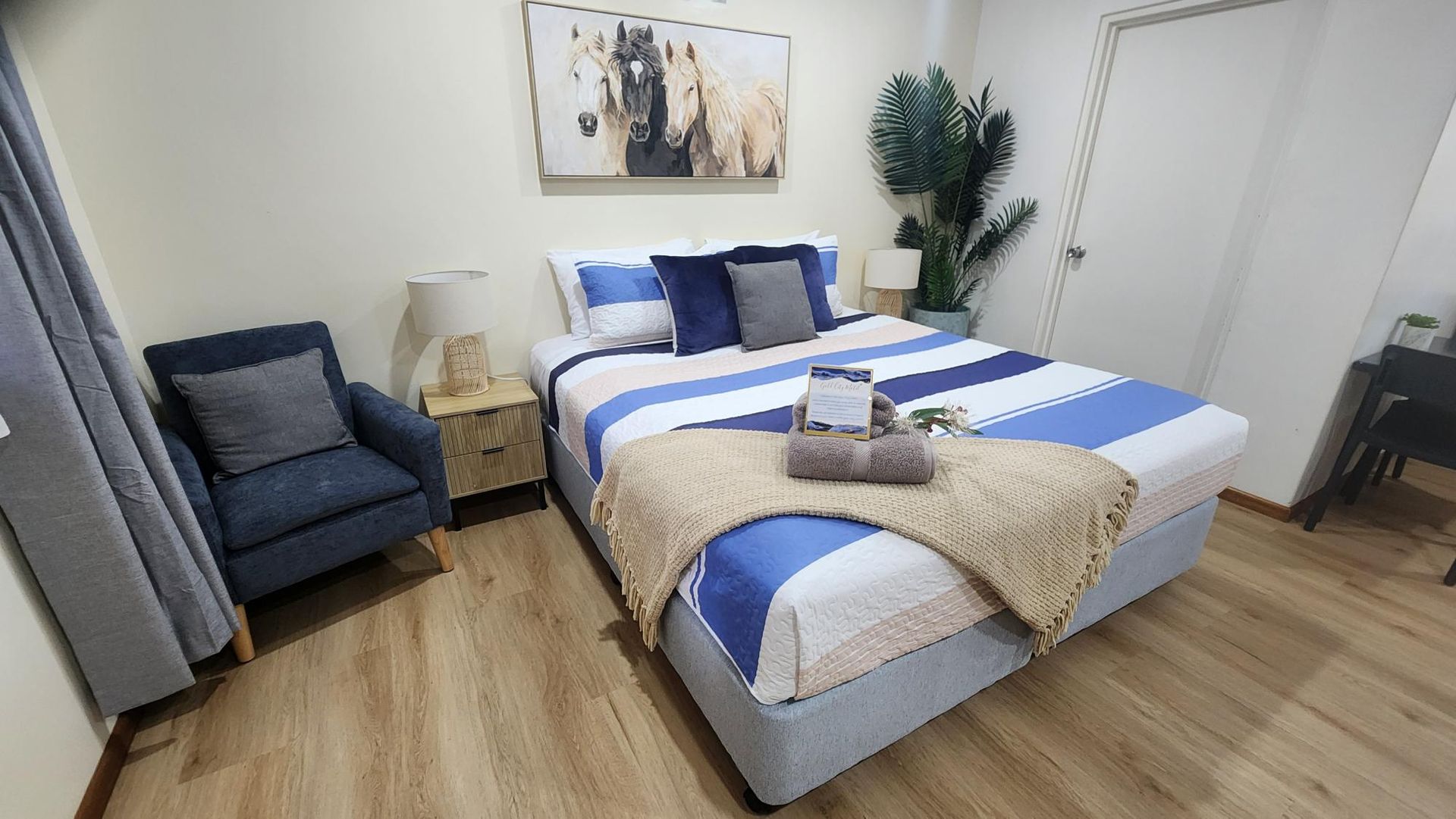 Compact studio room with two beds, bar stools, ceiling fan, TV, kitchenette, and open bathroom door