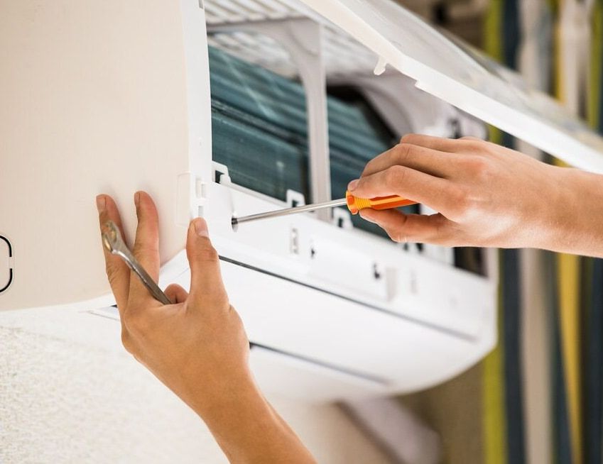 A Person Is Fixing An Air Conditioner With A Screwdriver — Ramm Air Conditioning In Port Macquarie, NSW