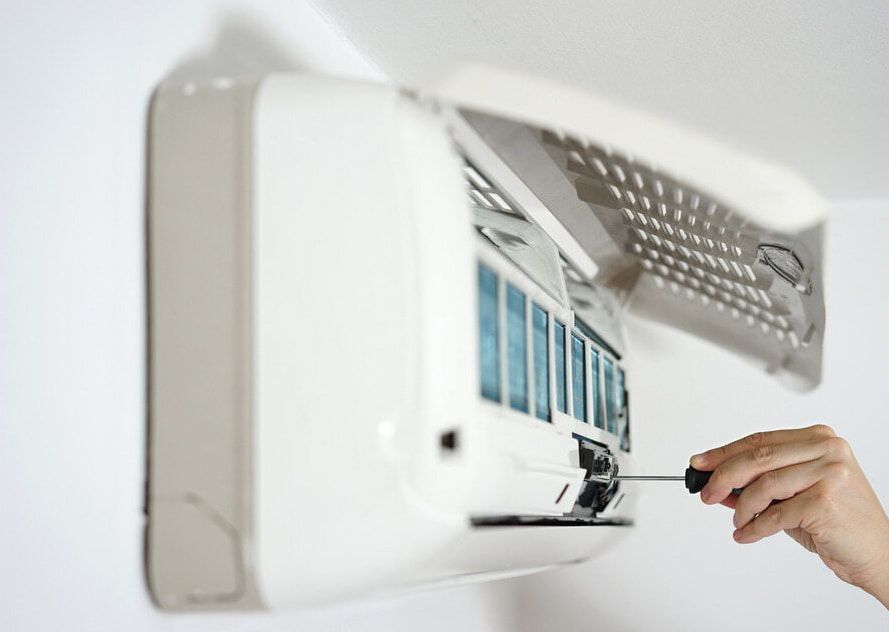 A Person Is Fixing An Air Conditioner With A Screwdriver — Ramm Air Conditioning In Port Macquarie, NSW