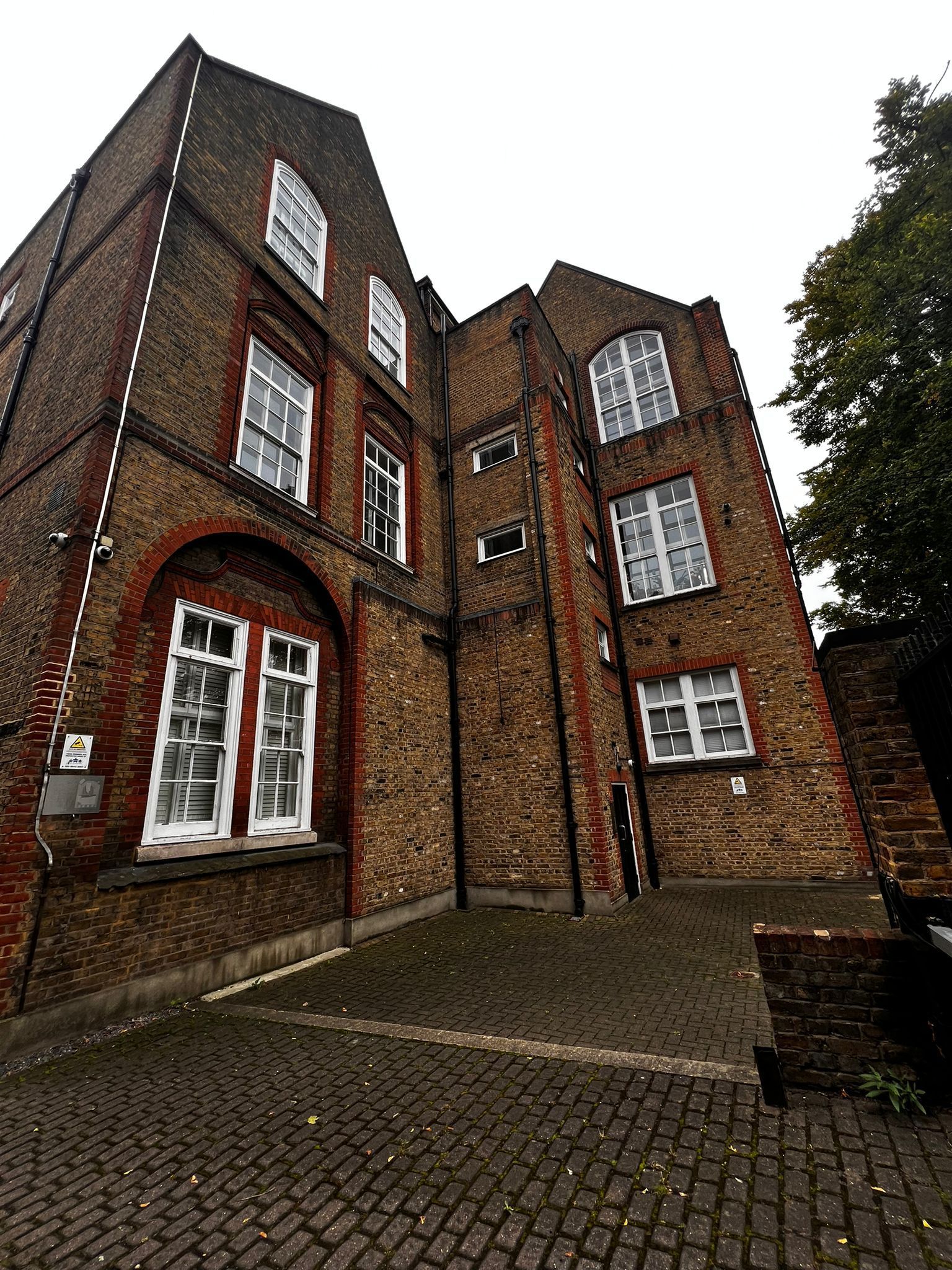 A large brick building with a lot of windows and a cobblestone driveway in front of it.