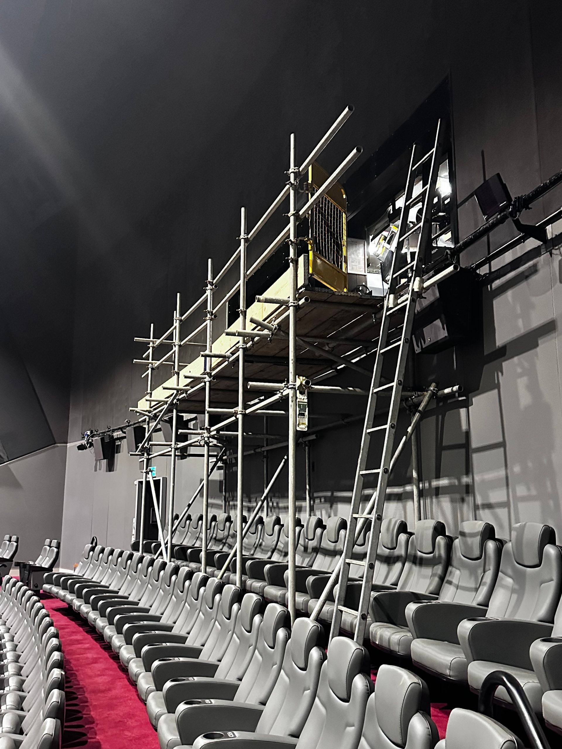 A row of empty seats in a theater with scaffolding on the wall.