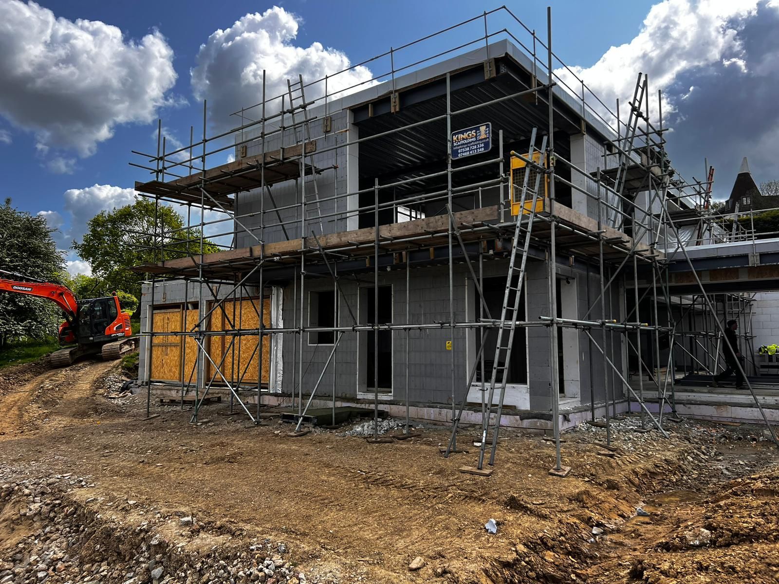 A house is being built with scaffolding and an excavator in the background.