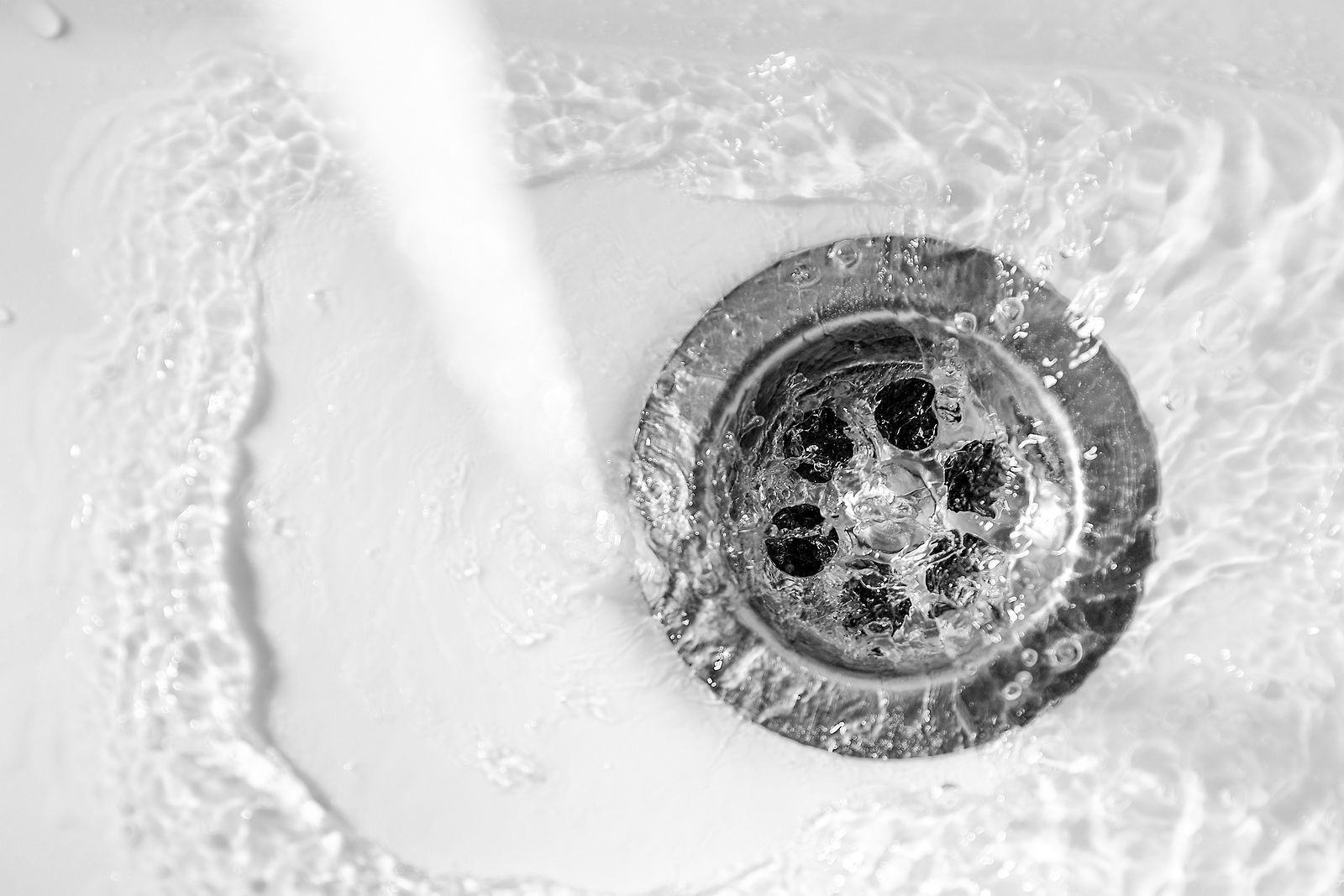 A black and white photo of water running down a sink drain.