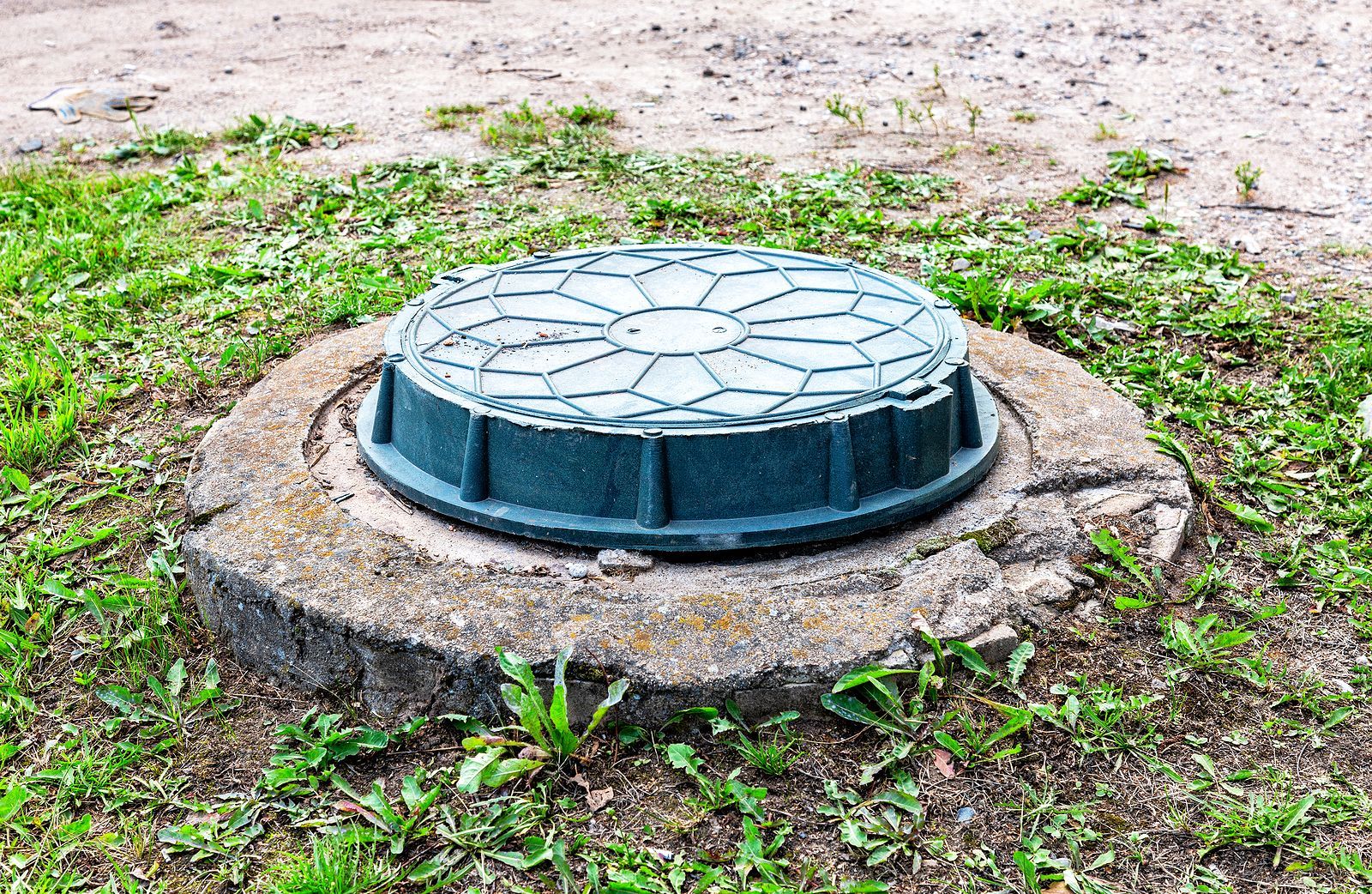 A manhole cover is sitting on top of a concrete circle in the grass.