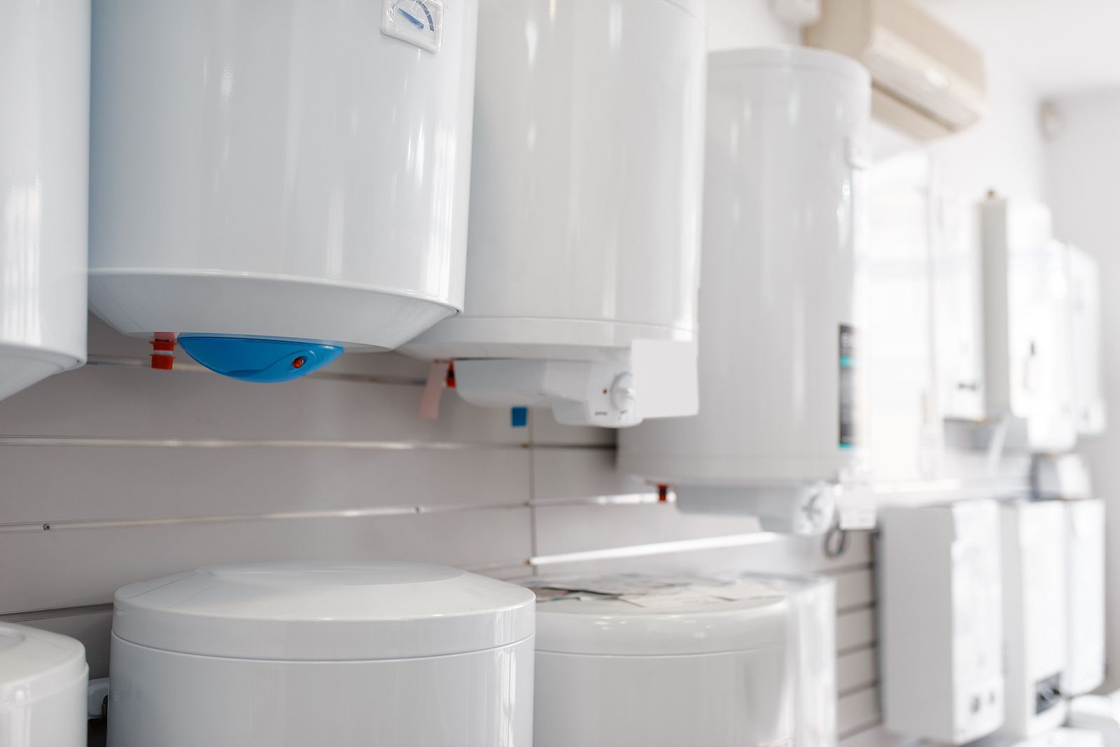 A row of white water heaters hanging on a wall in a store.