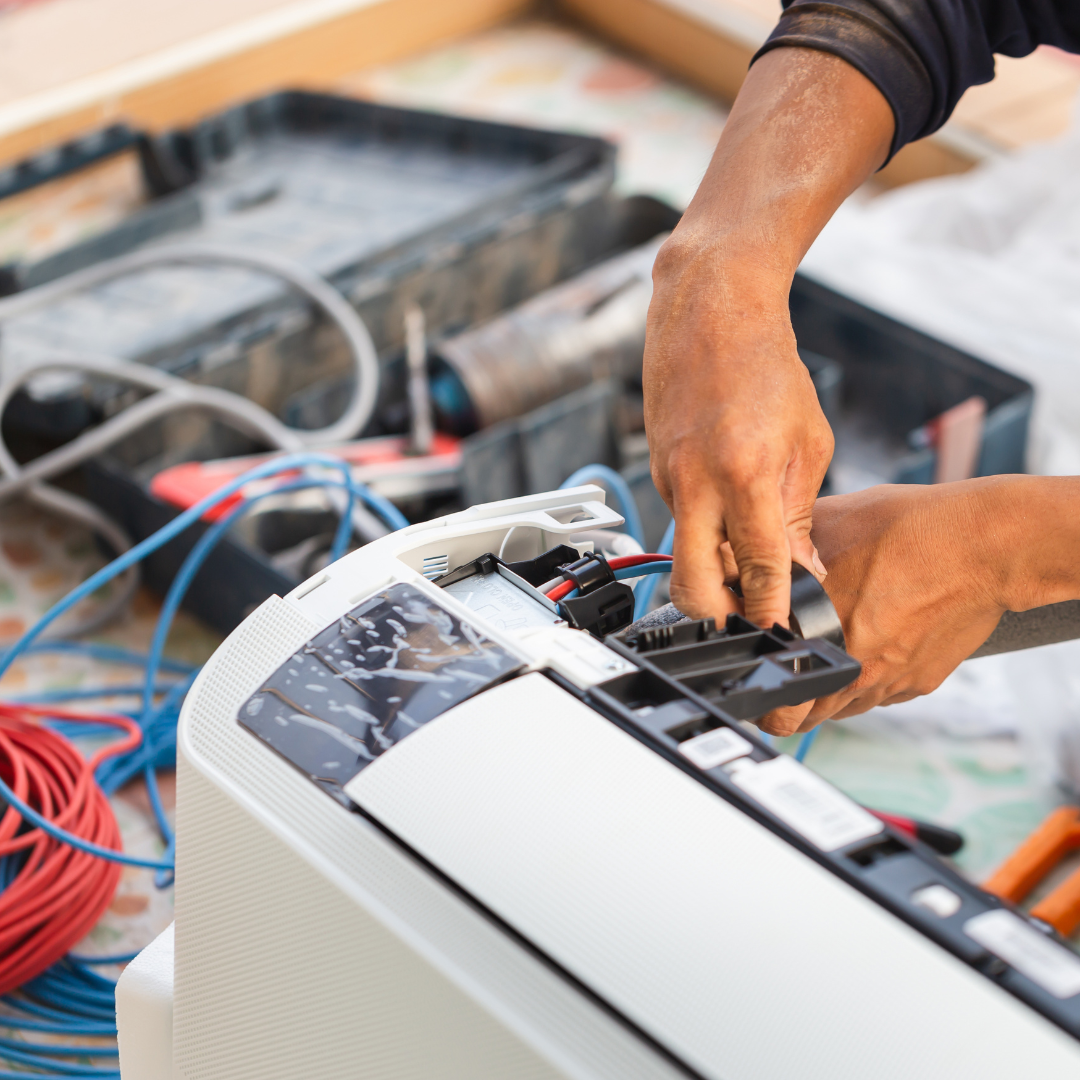 A man is working on an air conditioner with a pair of pliers