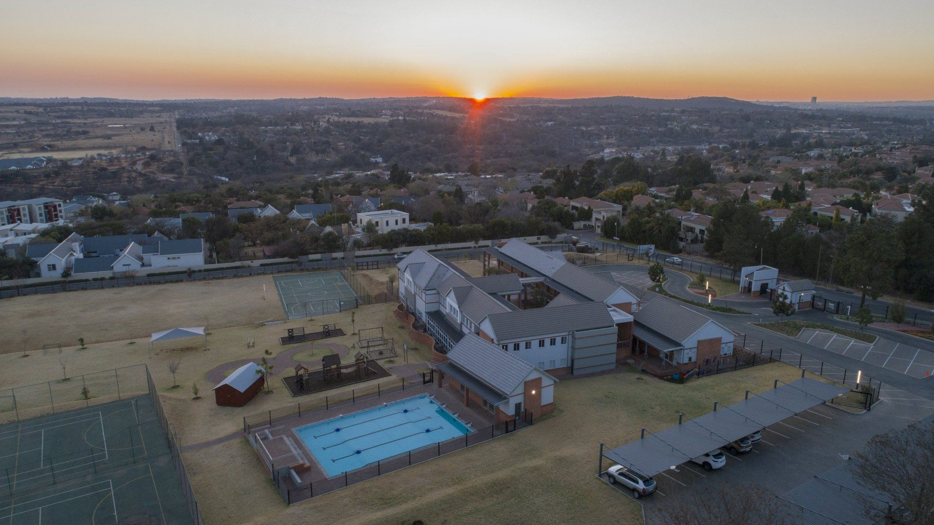 An aerial view of a school with a swimming pool at sunset.