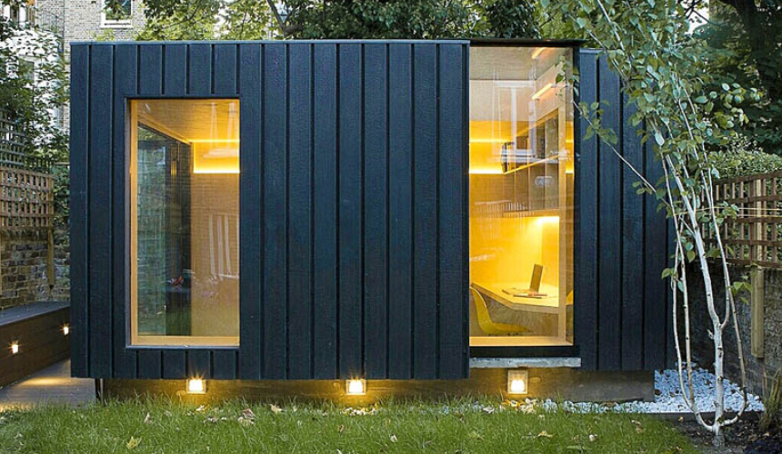 A sleek, modern garden cabin with black timber cladding, warm interior lighting, and large windows, blending style and functionality.