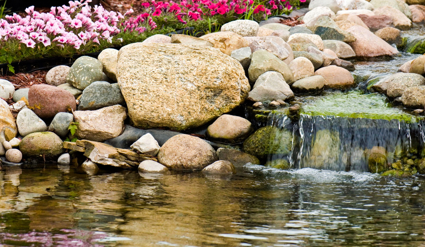 A gentle, sloping waterfall meanders through lush planting, gracefully leading into a peaceful garden pond—a harmonious blend of nature and design.