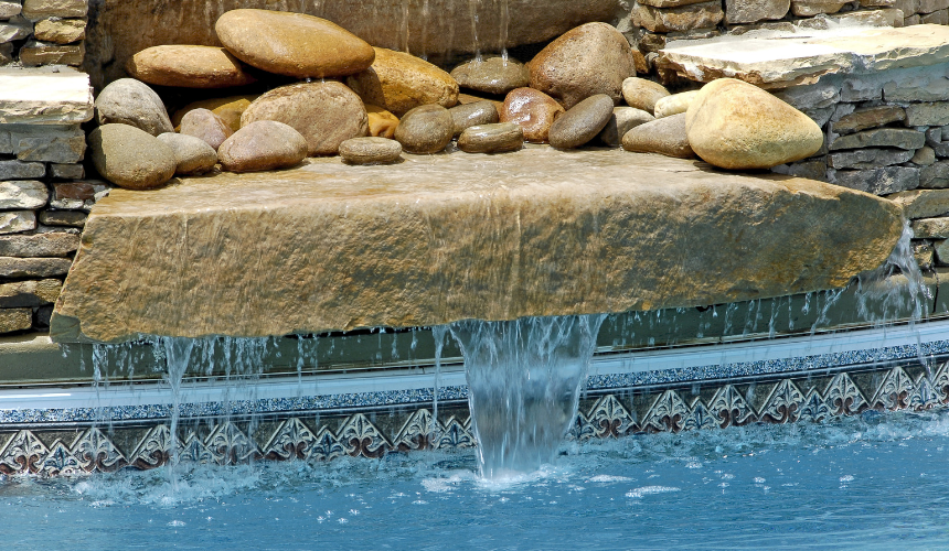 An aquascape of rocks and a waterfall cascading into a swimming pool - hardscaping imagined by Greenway.