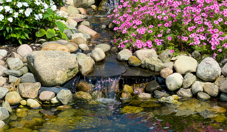 A picturesque rock garden waterfall surrounded by vibrant plants and flowers, creating a harmonious blend of natural beauty and tranquil water features.