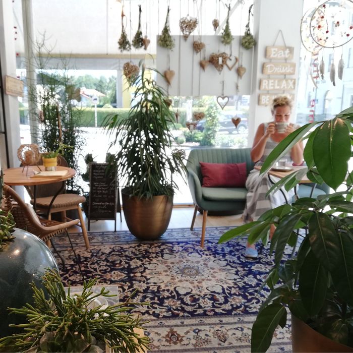 Eine Frau sitzt in einem Raum mit vielen Pflanzen und einer Tasse Kaffee