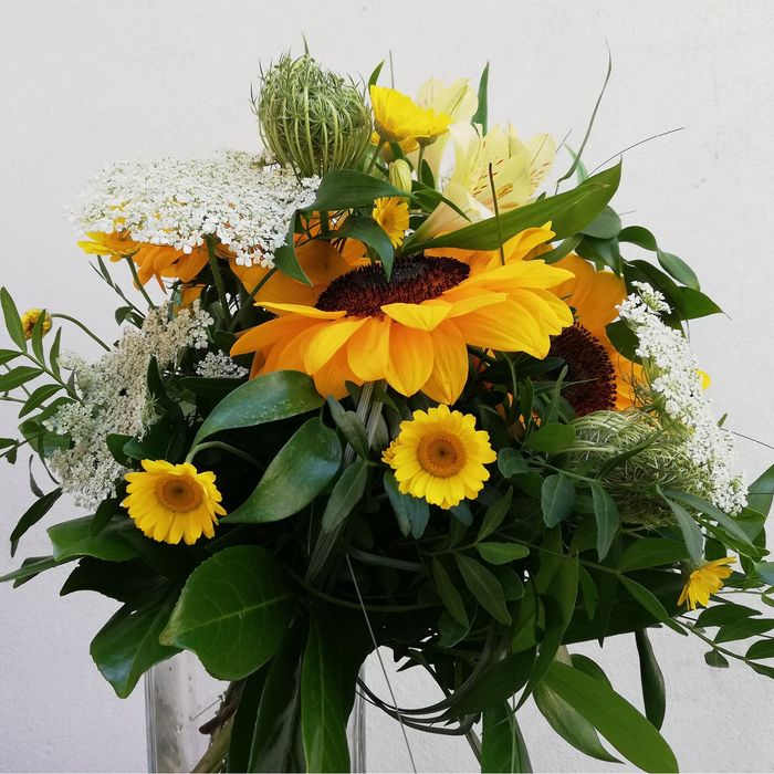 ein Blumenstrauß mit Sonnenblumen und weißen Blüten in einer Glasvase
