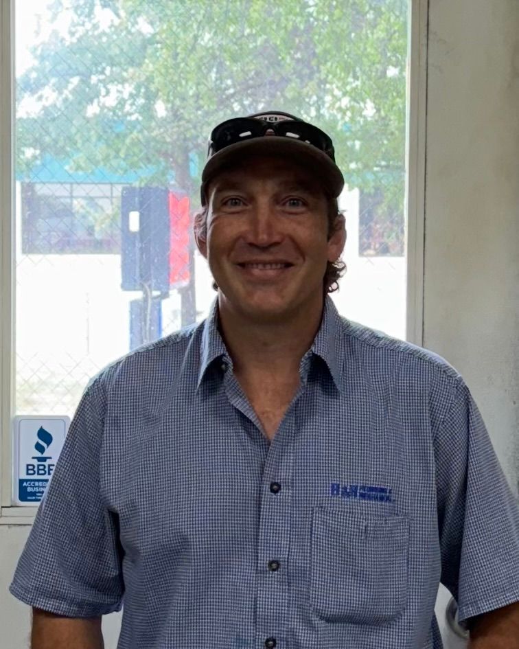 A man wearing a hat and a blue shirt is standing in front of a window.