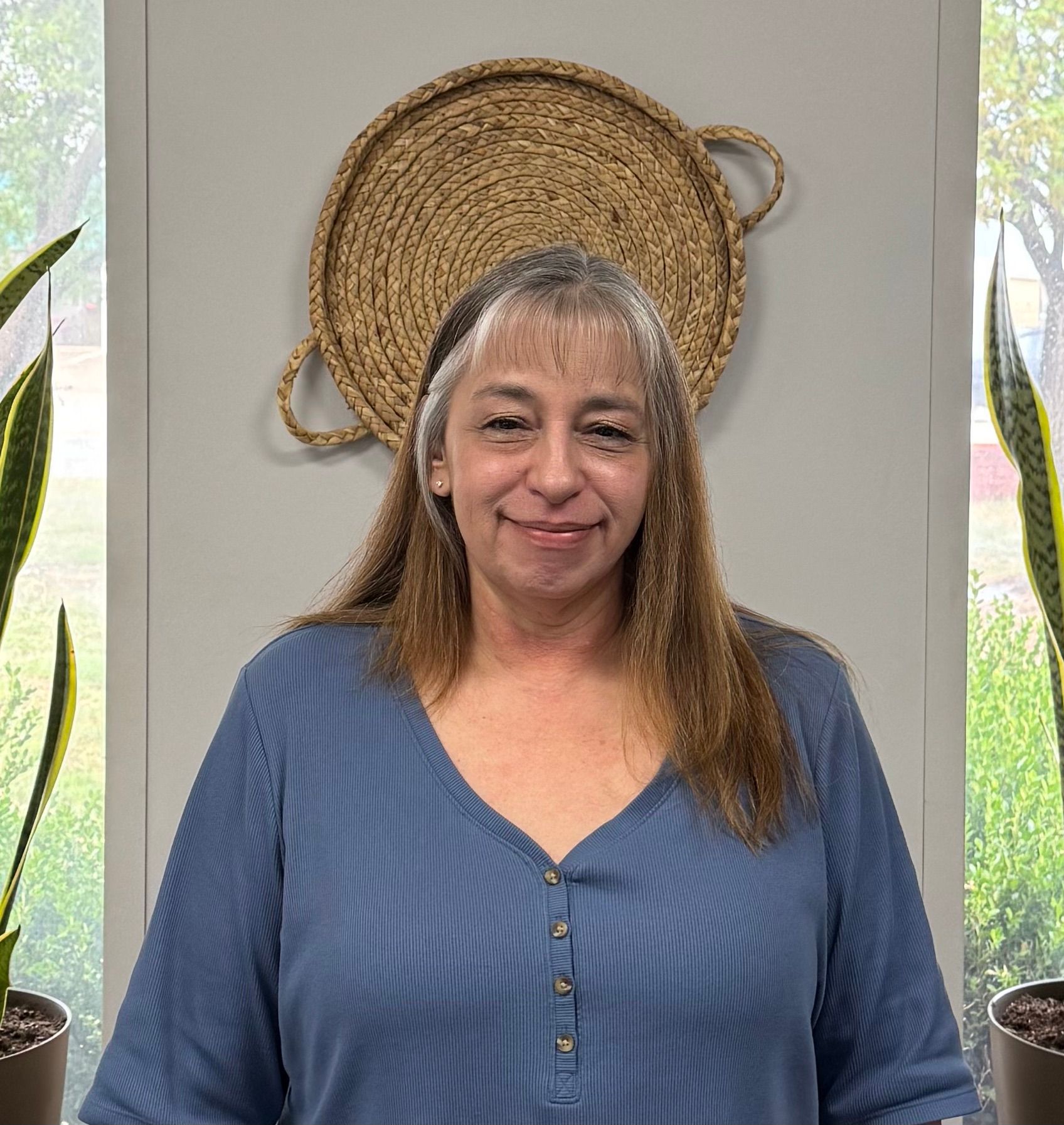 A woman in a blue shirt is standing in front of two potted plants.