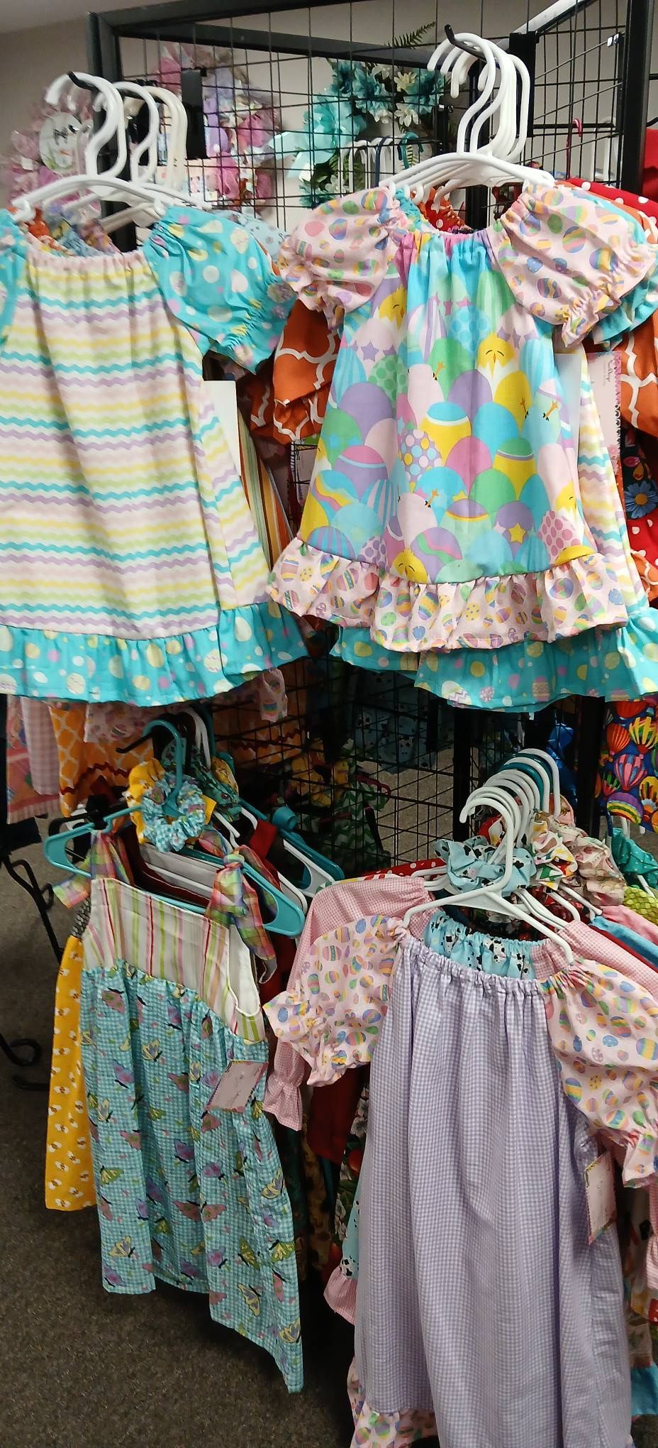 Colorful children’s dresses hanging on a market rack, with pastel stripes, florals, and gingham patterns.