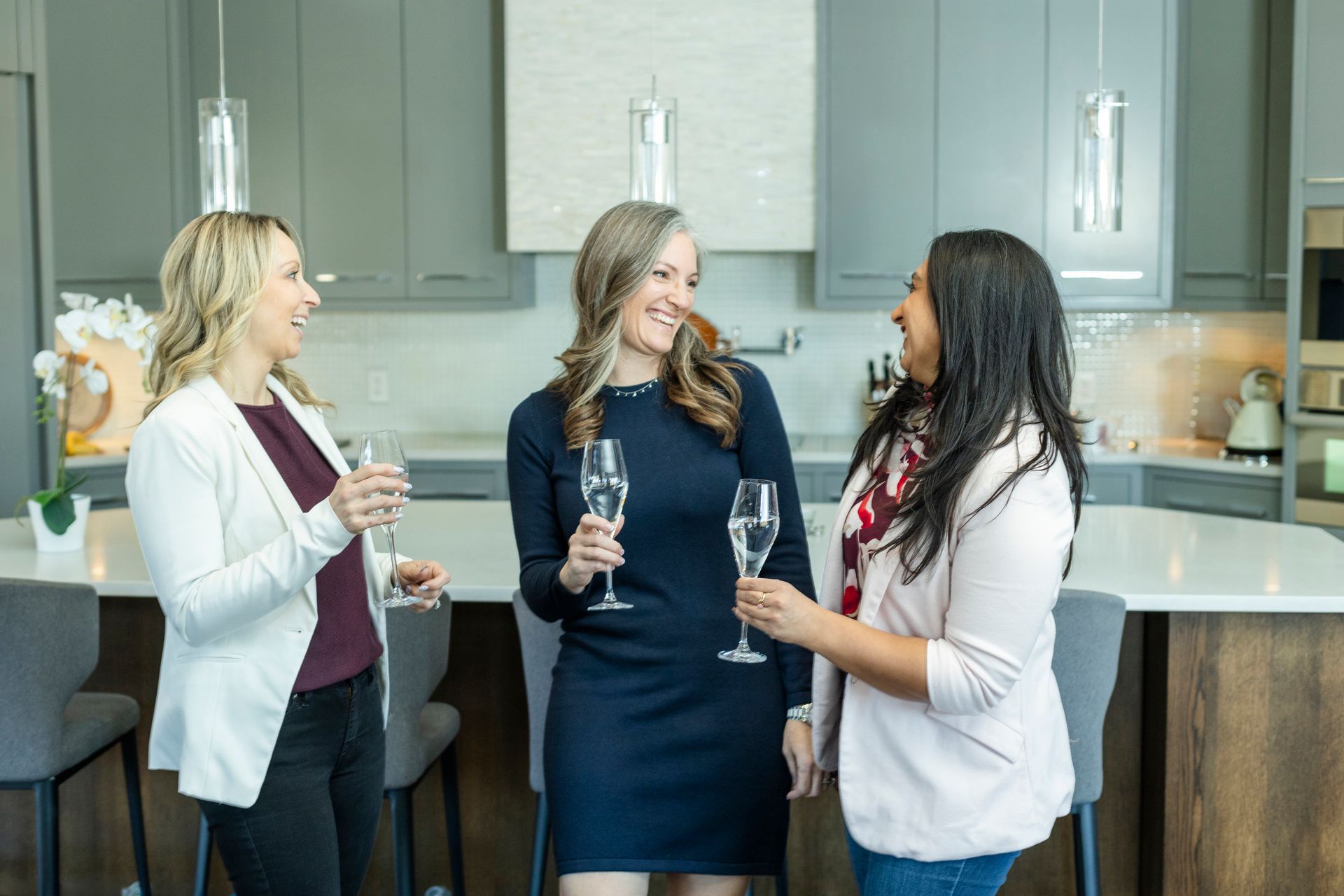 Three women are standing in a kitchen holding champagne glasses.