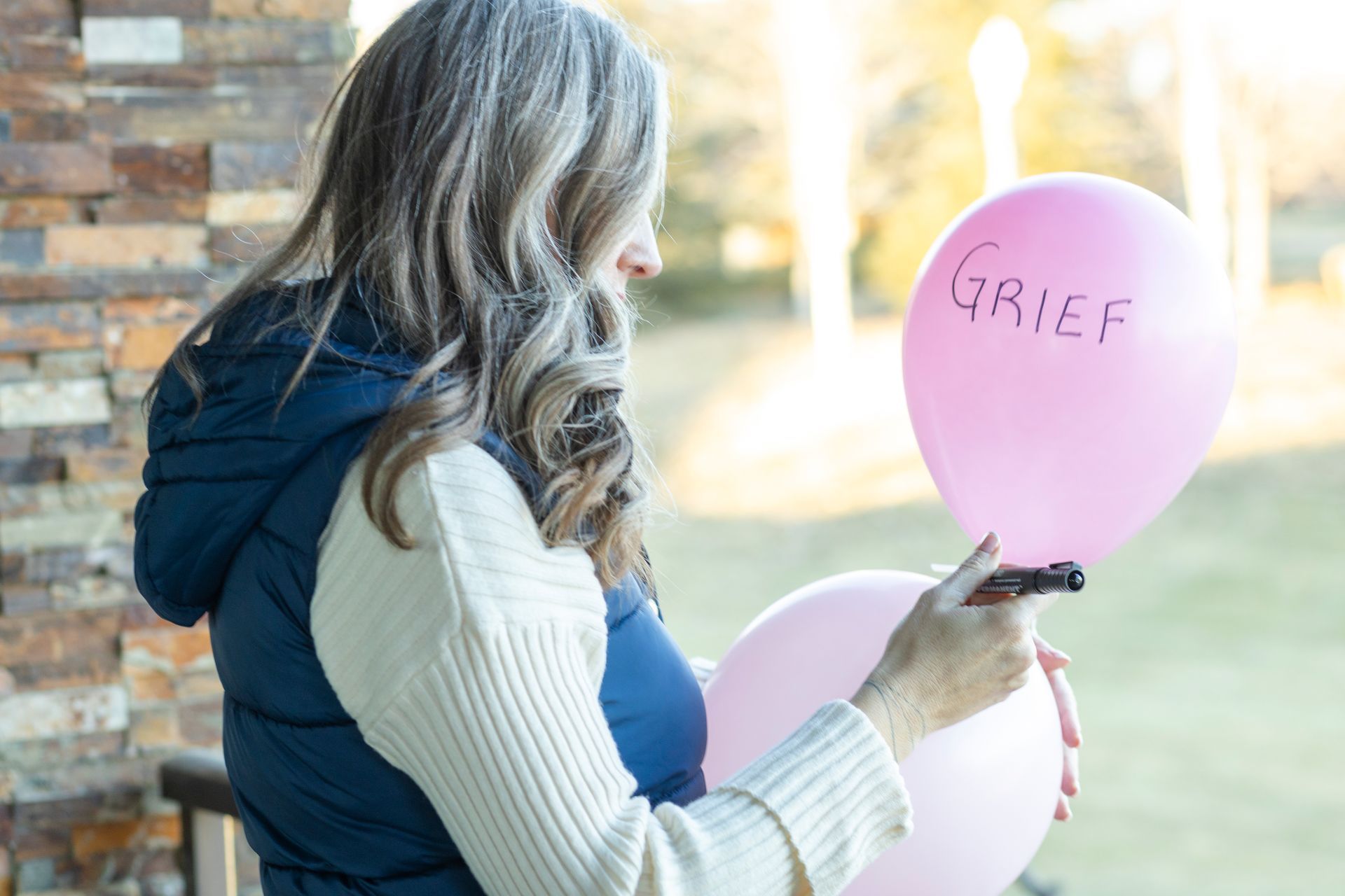 A woman is holding two pink balloons with grief written on them.