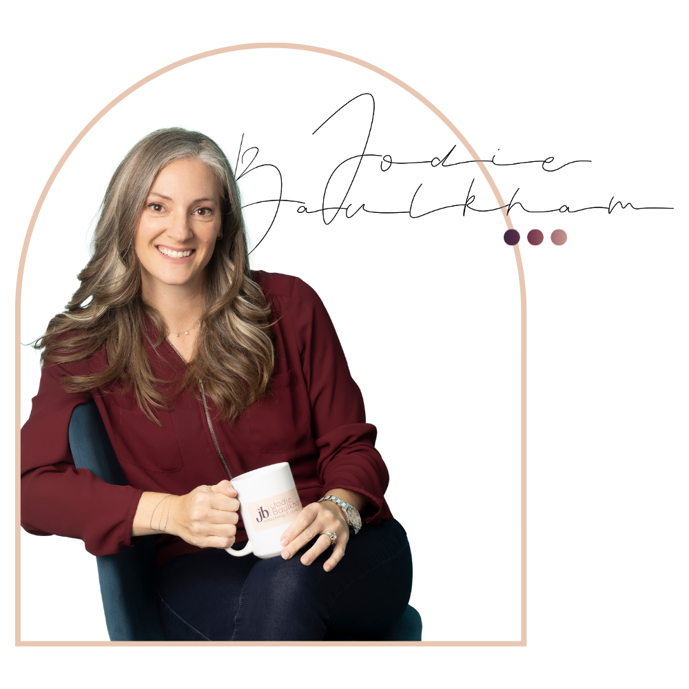 Jodie is sitting in a chair holding a mug and smiling.