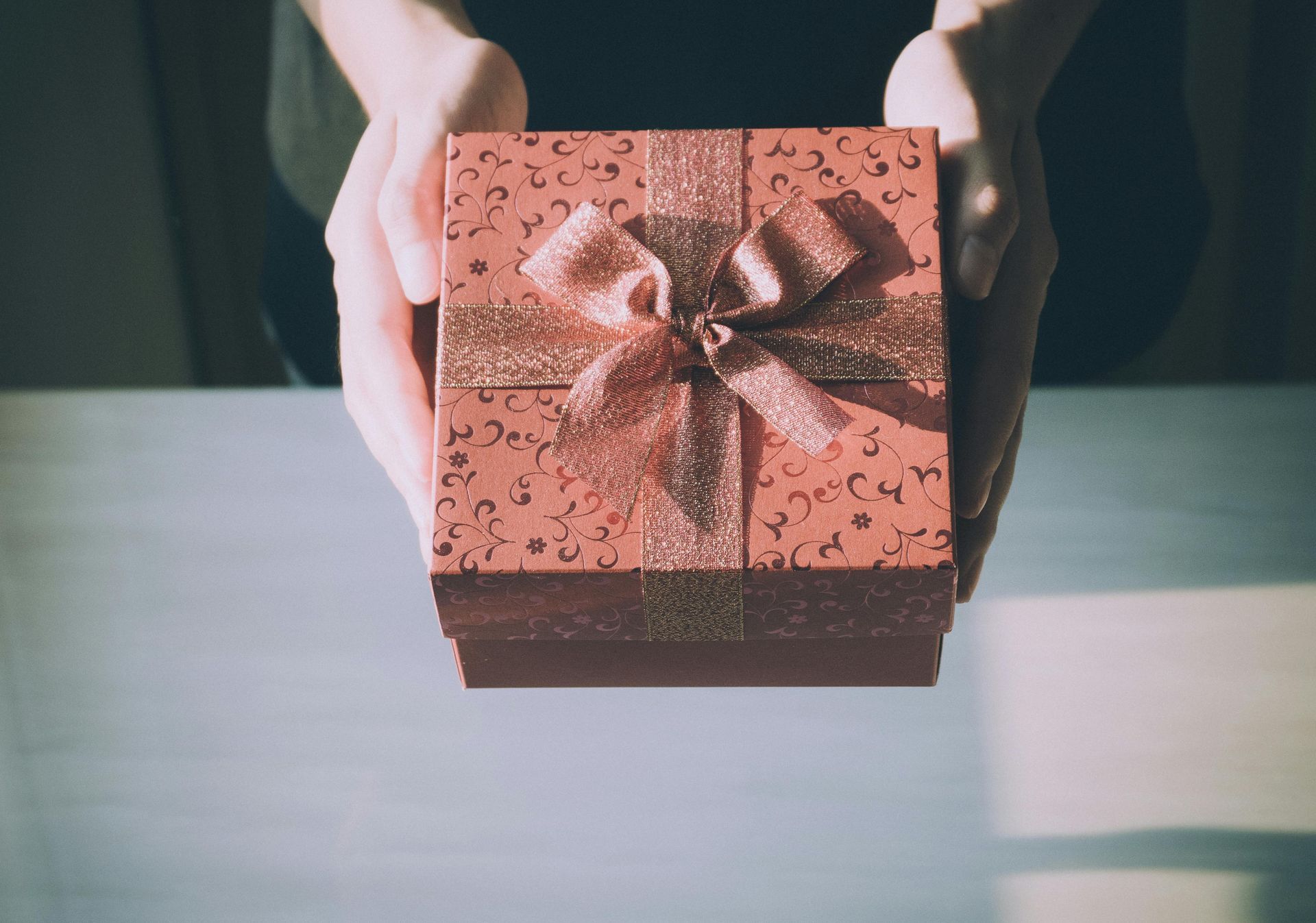 Two hands holding a gift wrapped in pink paper and bow