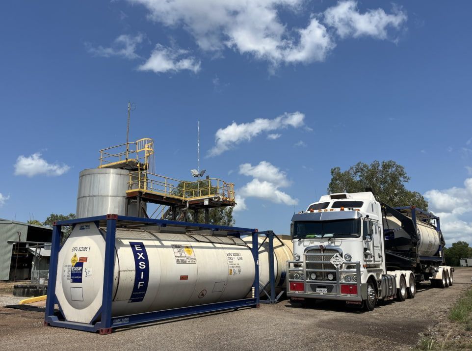 A Truck is Driving Down a Dirt Road Next to a Large Tank — Harker Haulage In Humpty Doo, NT A Truck is Driving Down a Dirt Road Next to a Large Tank — Harker Haulage In Humpty Doo, NT