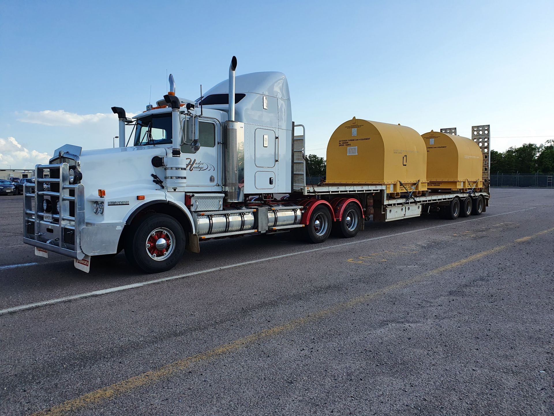 White semi-truck hauling two yellow containers on a flatbed trailer in a parking lot. — Harker Haulage In East Arm, NT
