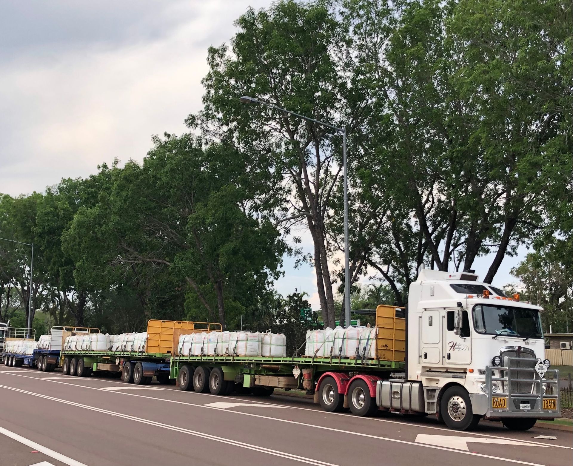 Semi-trucks hauling freight on a road, lined with trees. — Harker Haulage In East Arm, NT