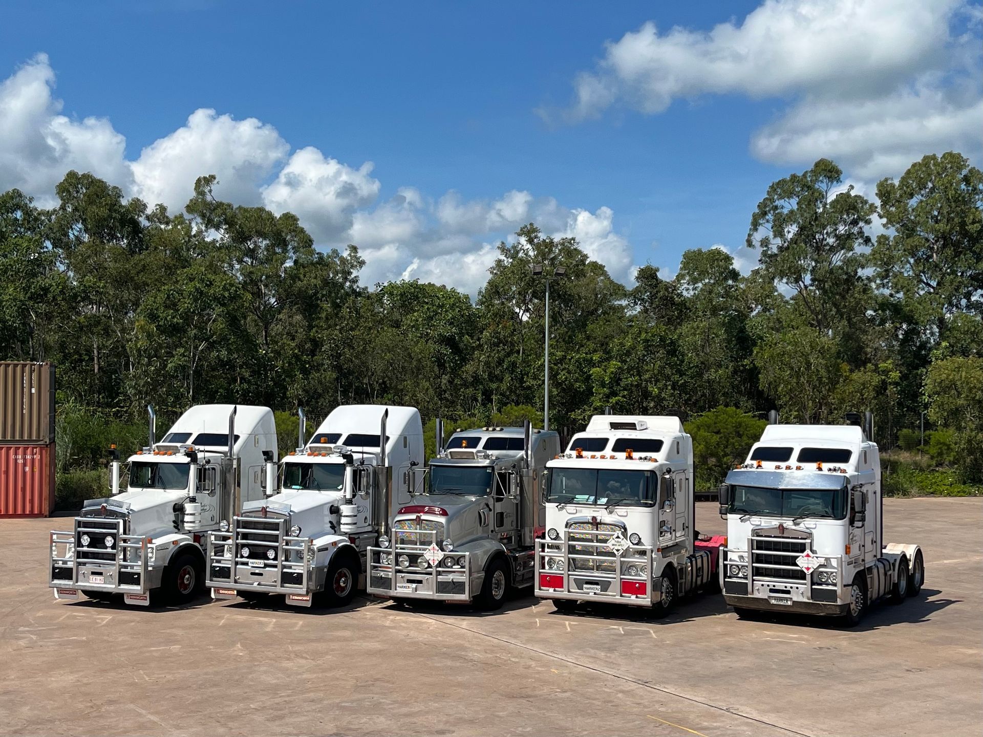 Five white semi-trucks parked outdoors under a blue sky with trees in the background. — Harker Haulage In East Arm, NT