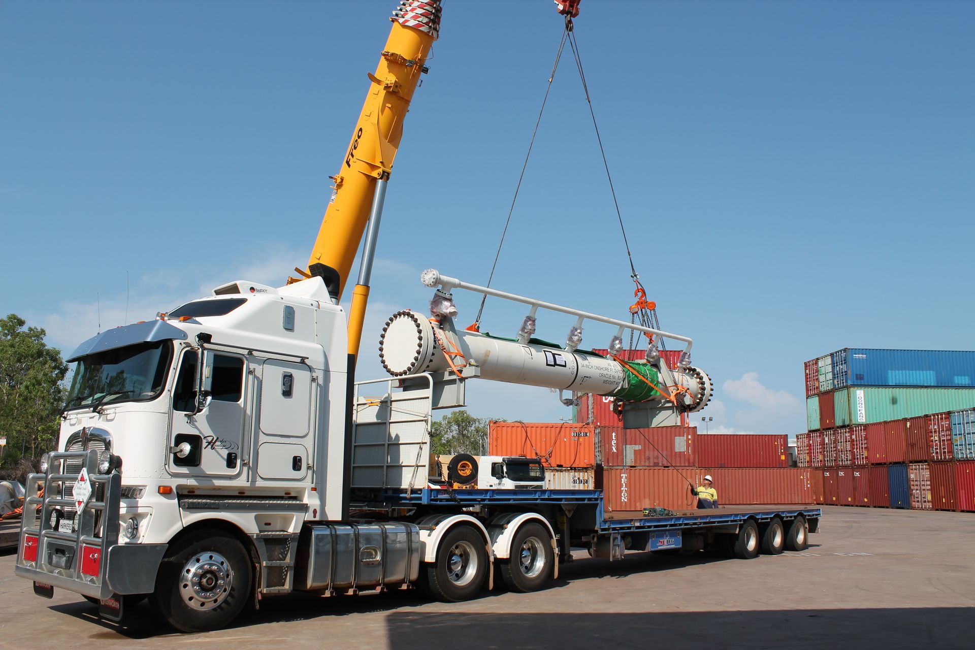 A large white truck with a crane lifting a long, cylindrical object in a cargo area. — Harker Haulage In East Arm, NT