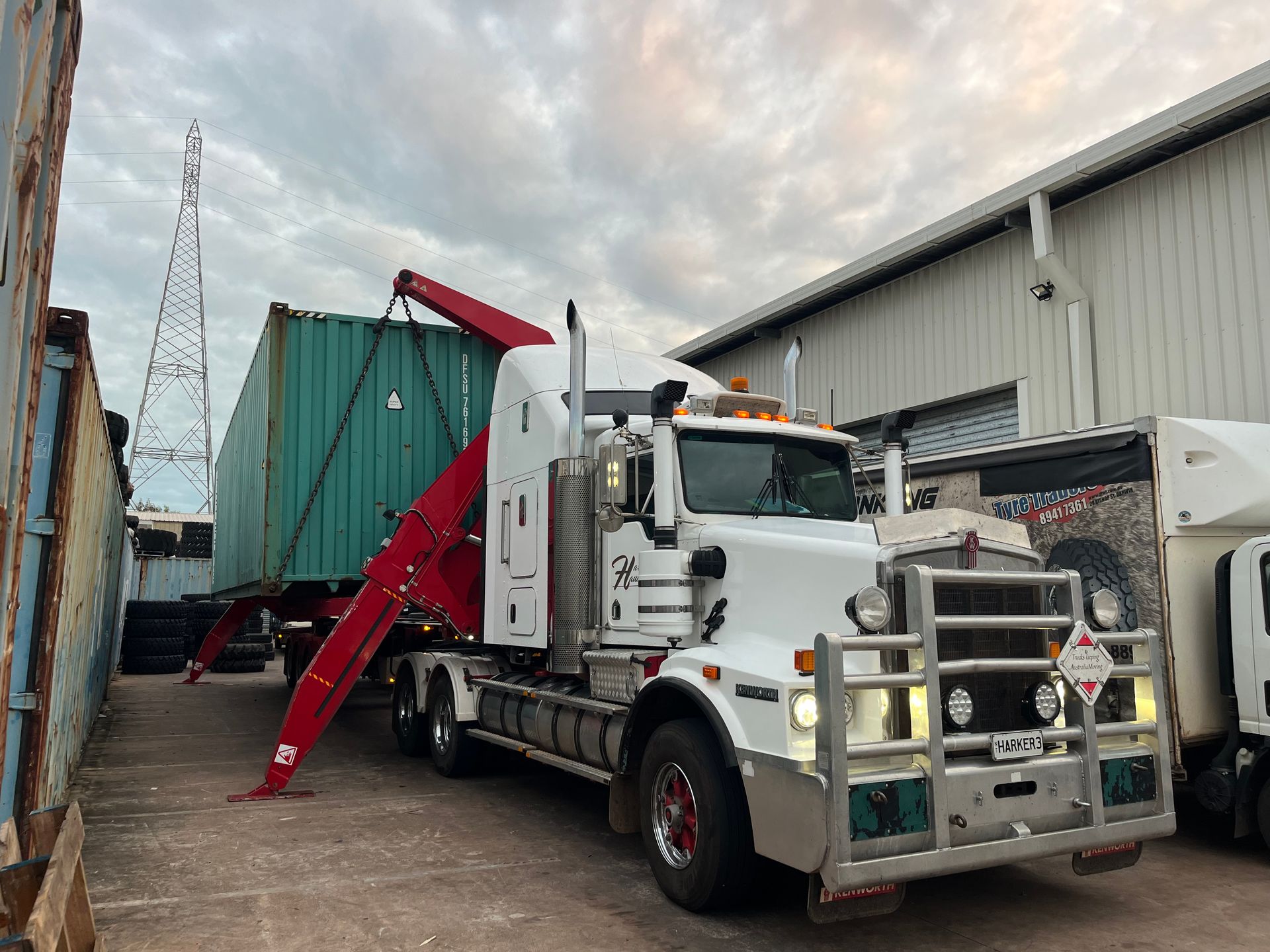 White semi-truck with red crane lifting a green shipping container in an urban setting. — Harker Haulage In East Arm, NT