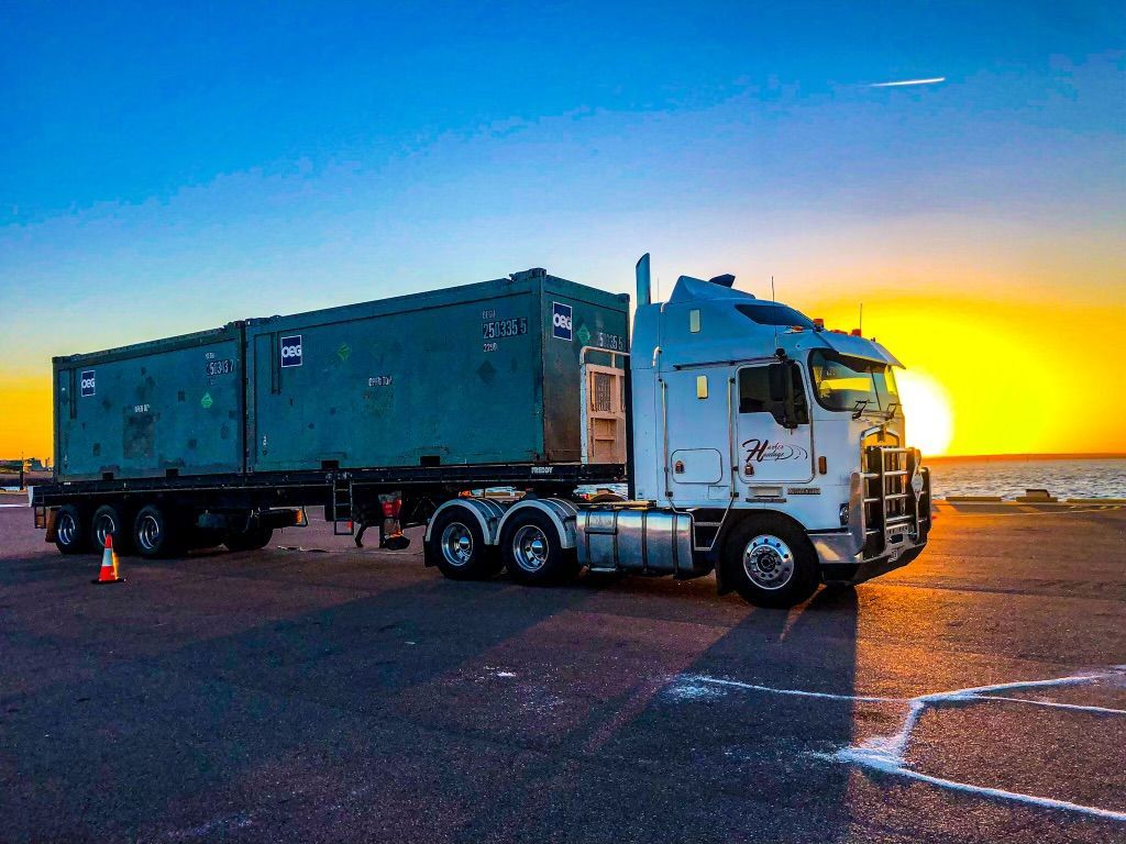 Semi-truck with a container on a trailer parked on a pier, sun setting in the background. — Harker Haulage In East Arm, NT