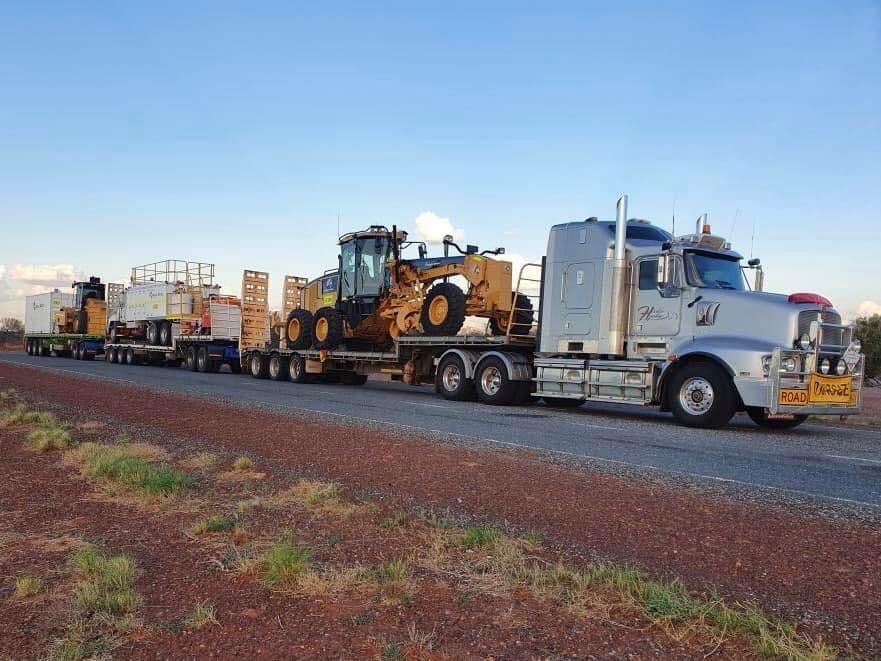 A semi-truck hauling heavy machinery on a long, red dirt road; sunny day. — Harker Haulage In East Arm, NT