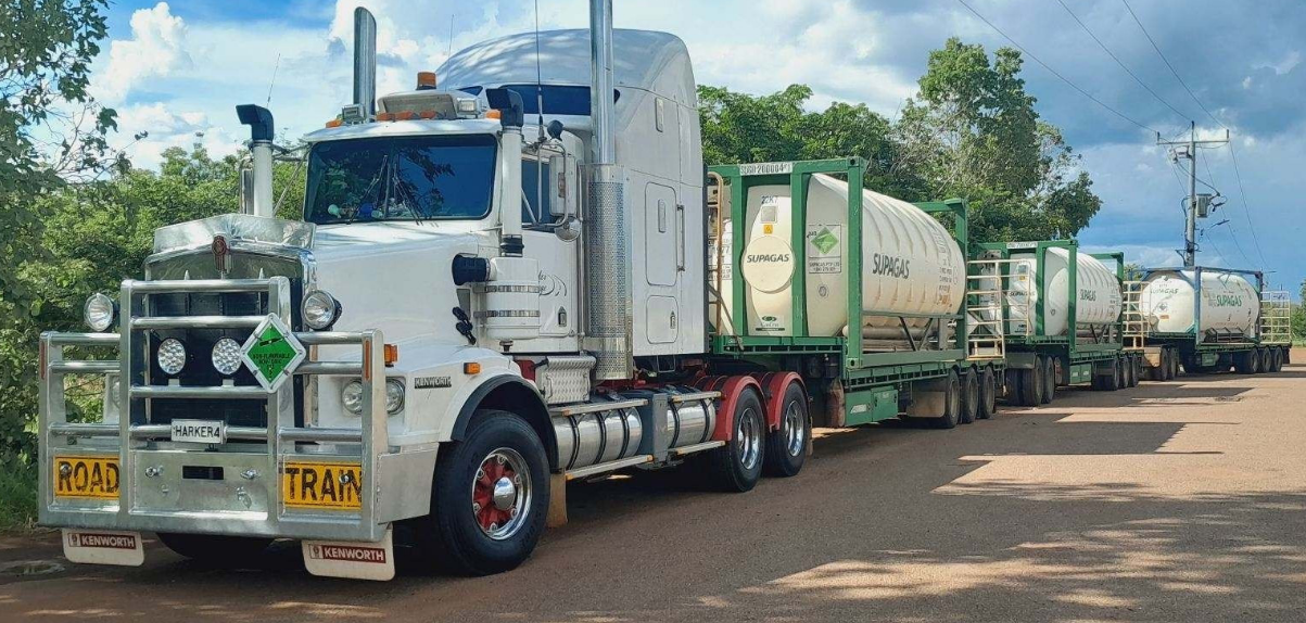 A White Semi Truck is Driving Down a Dirt Road Next to a Row of Other Trucks — Harker Haulage In East Arm, NT