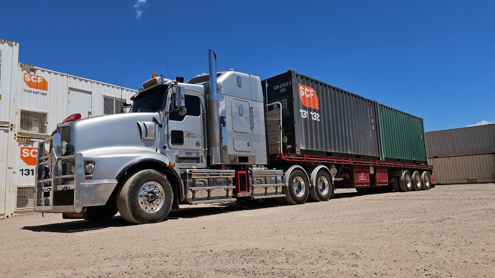 Silver semi-truck with two shipping containers on a gravel lot under a clear blue sky. — Harker Haulage In East Arm, NT