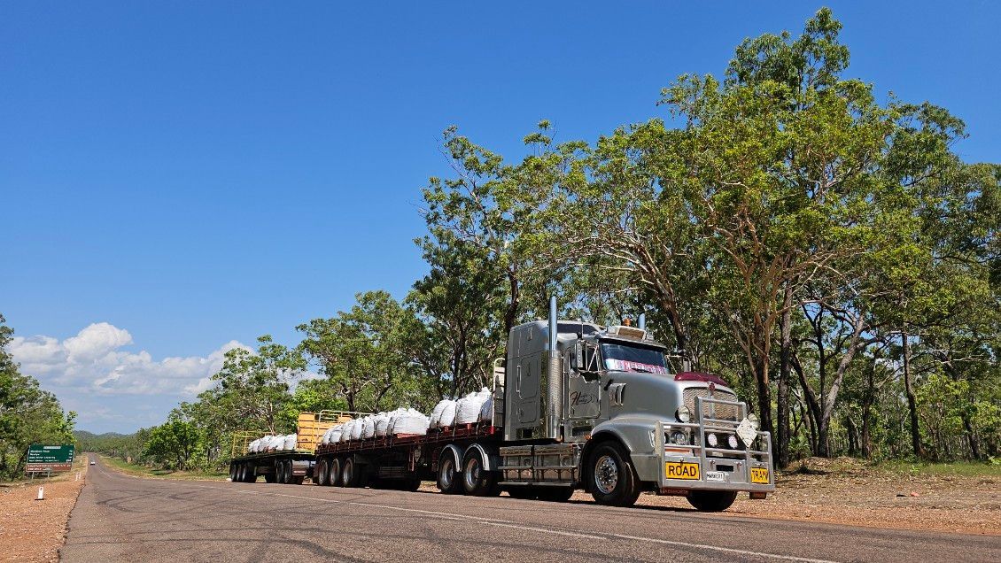 Semi-truck hauling a large load on a rural road under a bright blue sky, with trees on either side. — Harker Haulage In East Arm, NT