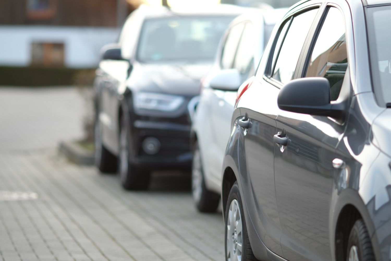 Coches aparcados en fila sobre una superficie de ladrillo, con el coche más cercano en foco.