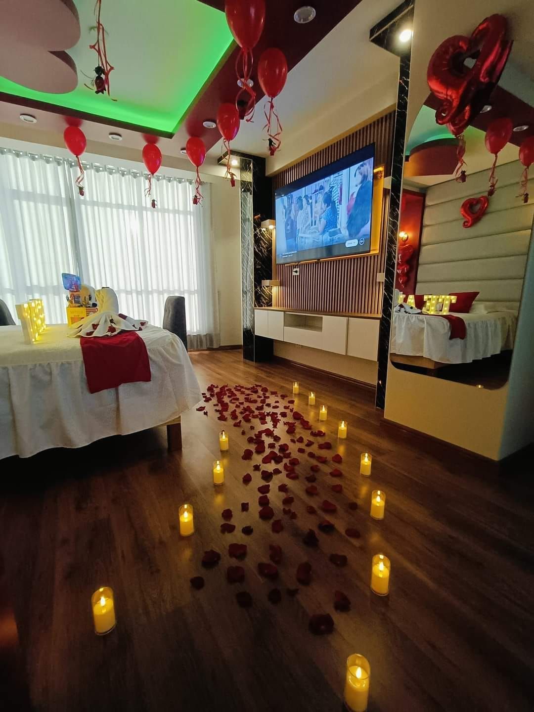Dormitorio romántico decorado con globos rojos, pétalos de rosa, velas y TV.