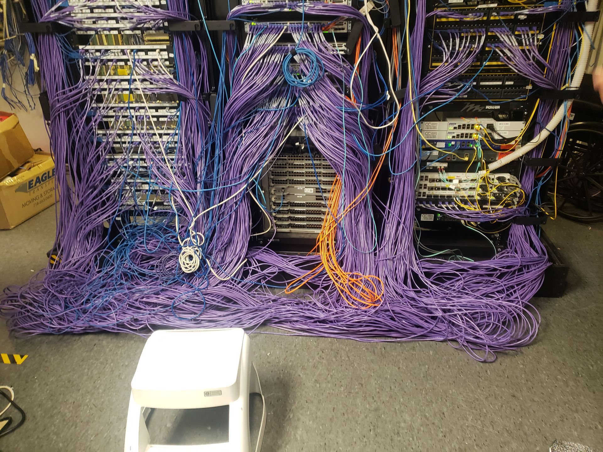 Server rack with tangled purple, blue, and orange network cables; a white step stool in front.
