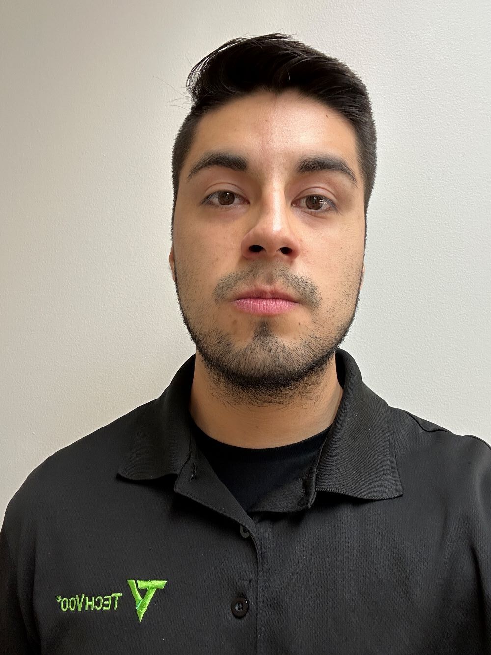 A man with a beard is wearing a black shirt with a green logo on it.