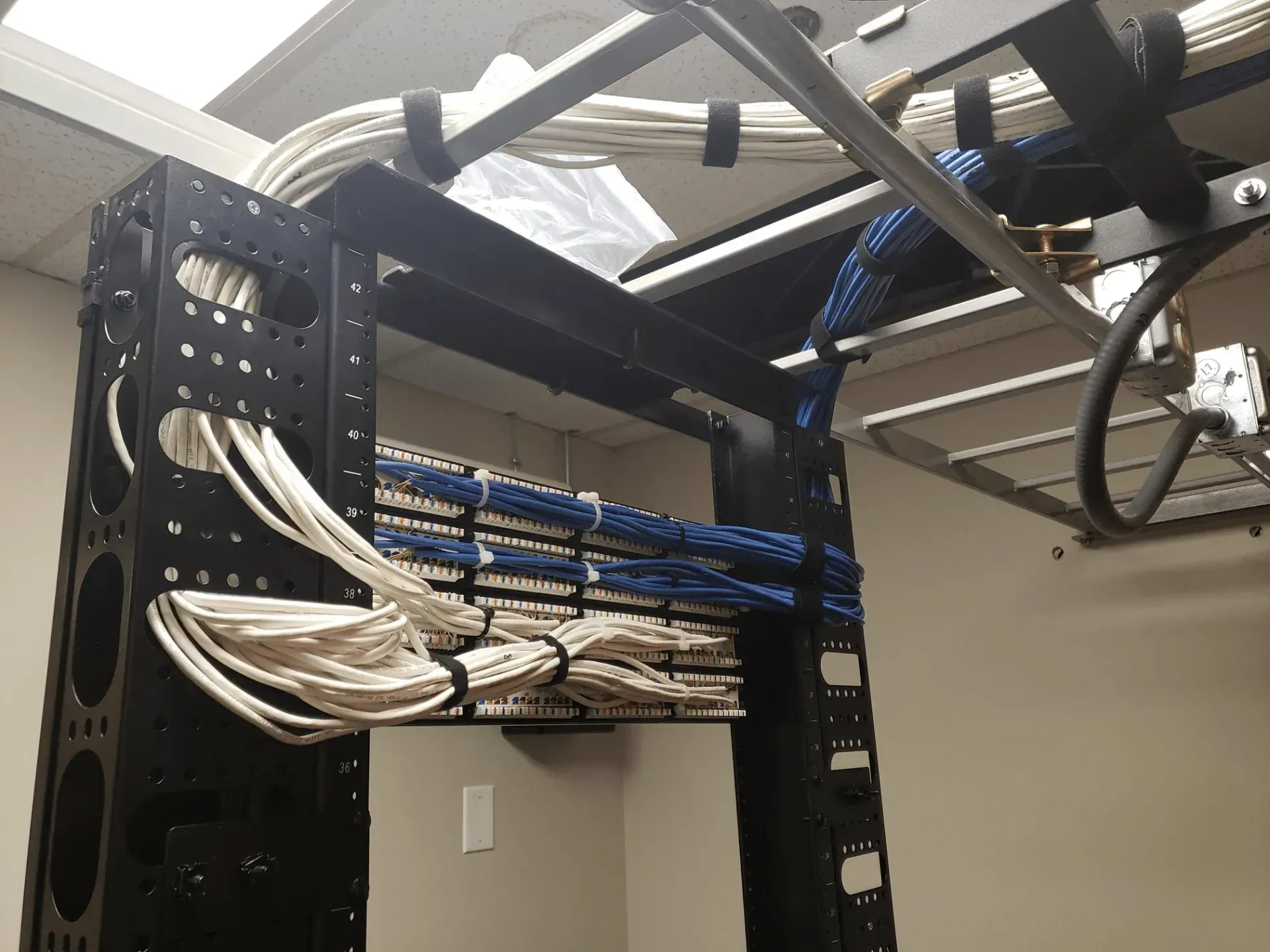 Black server rack with neatly organized network cables in a room with beige walls.