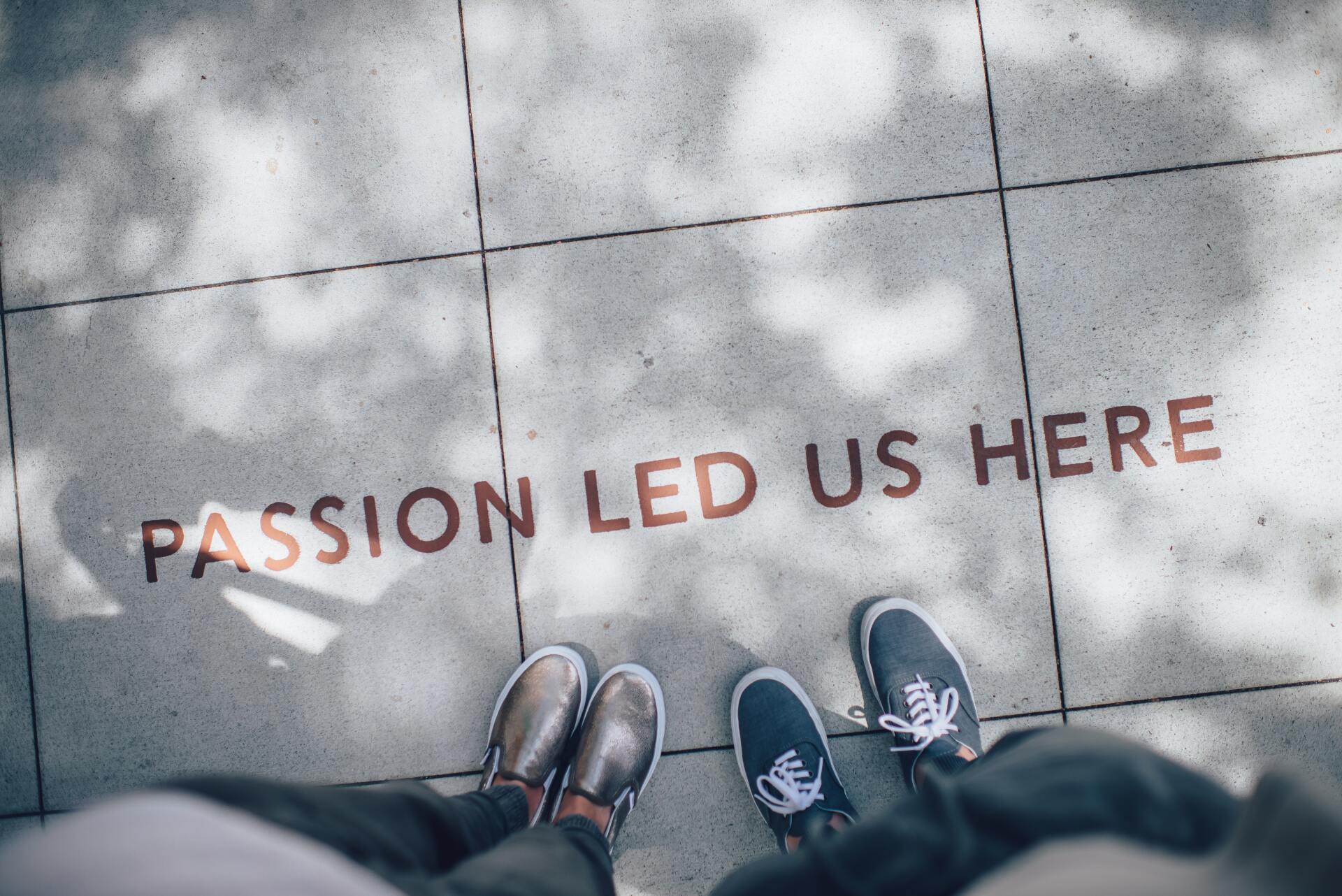 Two people are standing on a sidewalk with the words `` passion led us here '' written on the ground.