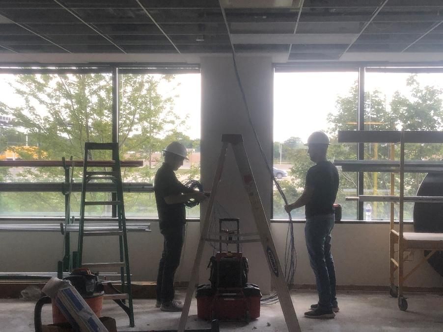 Two construction workers inside, installing drywall near windows.