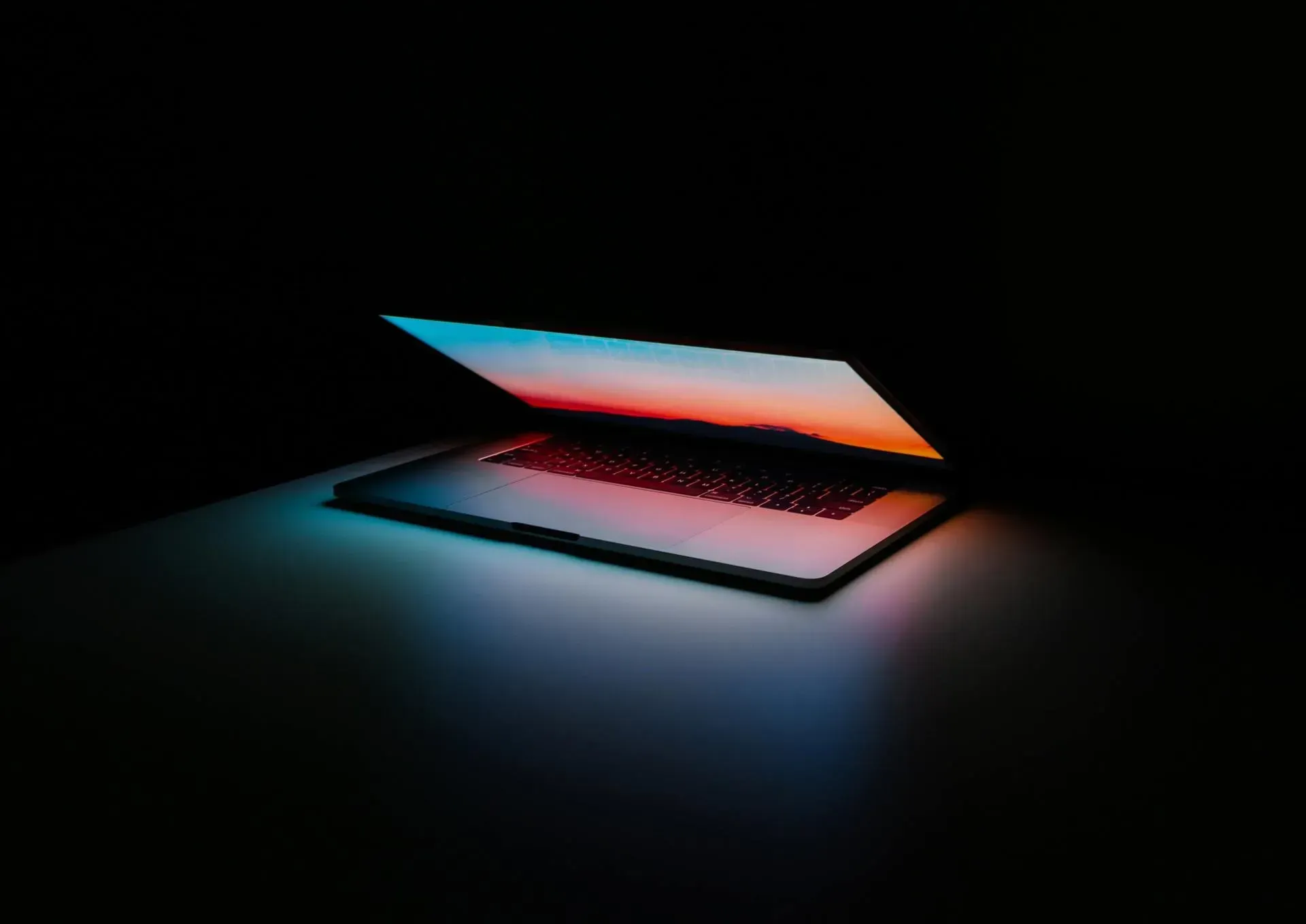 Laptop with screen glowing orange and blue in a dark setting, casting light onto the surface.