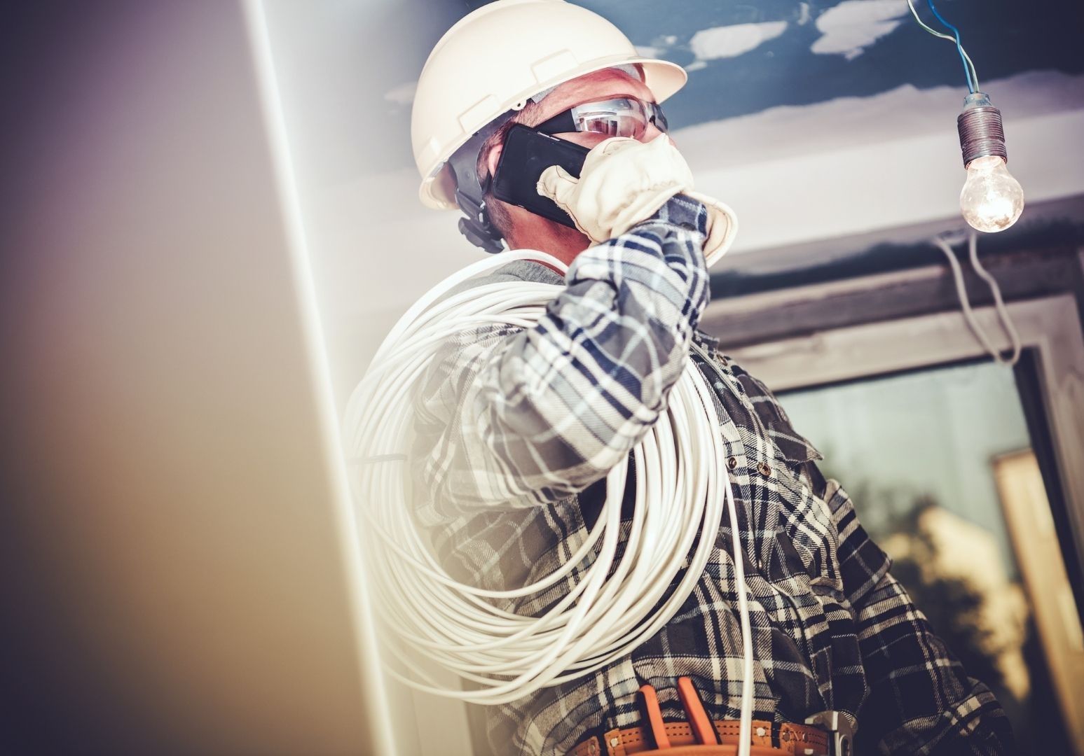 An electrician is talking on a cell phone while holding a roll of wires.