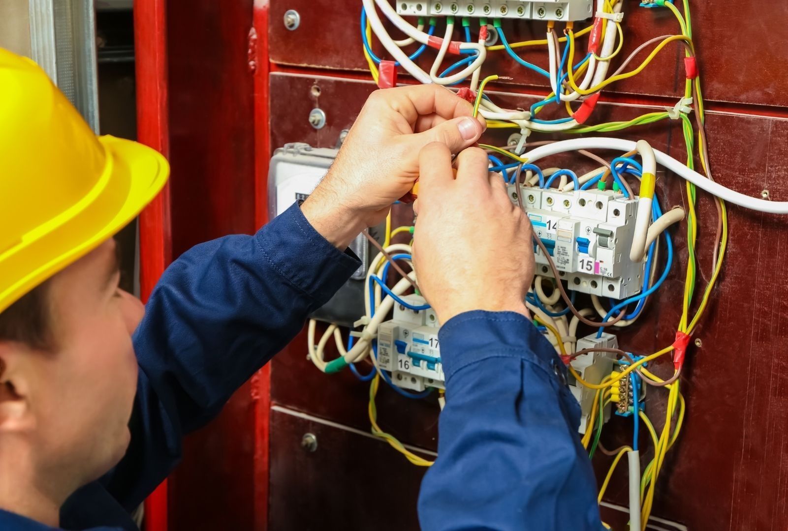 A man wearing a hard hat is working on an electrical panel.